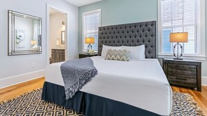 A bedroom with a large bed, two bedside lamps, a dark headboard, and a patterned rug.