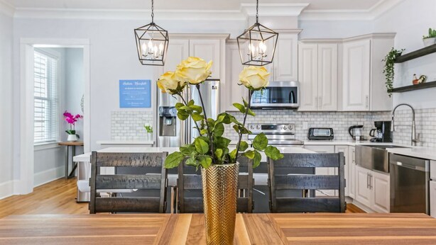 A modern kitchen with white cabinets, a wooden dining table, and a vase with yellow flowers.