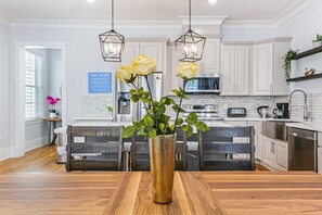 A modern kitchen with white cabinets, a wooden dining table, and a vase with yellow flowers. - Stunning 4 BR Condo + Pool - Near St. Charles (New Orleans)