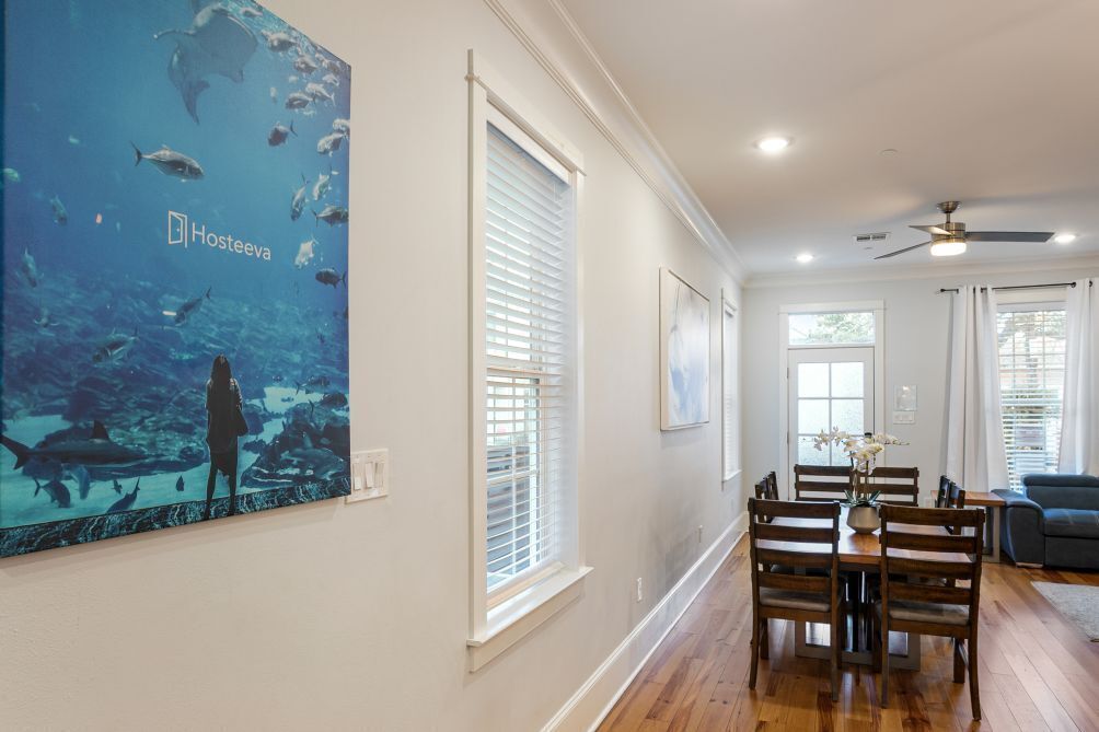 A spacious living room with a dining area, large windows with blinds, and a ceiling fan.