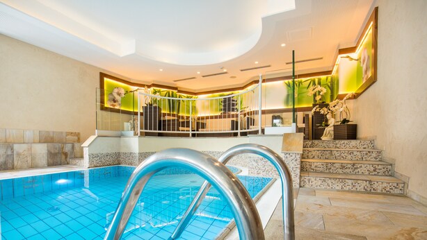 Ein Innenpool mit klaren blauen Fliesen, einer Metallleiter und einer Treppe, die zu einem Balkon mit Blick auf den Pool führt.