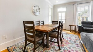 Un comedor con una mesa y sillas de madera, un tapete floral y un reloj de pared.