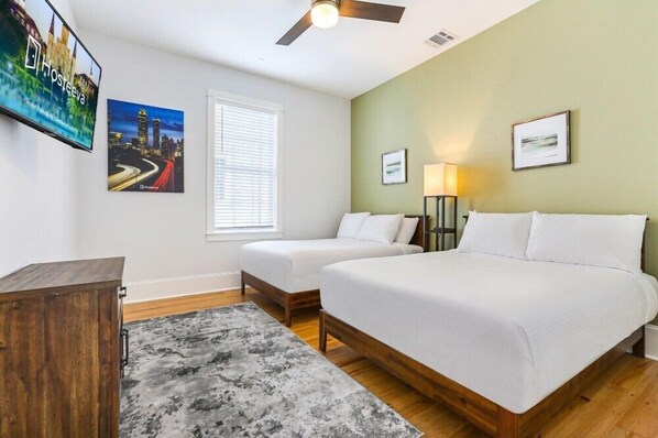 A hotel room with two beds, a wooden cabinet, a TV, and framed pictures on the wall.