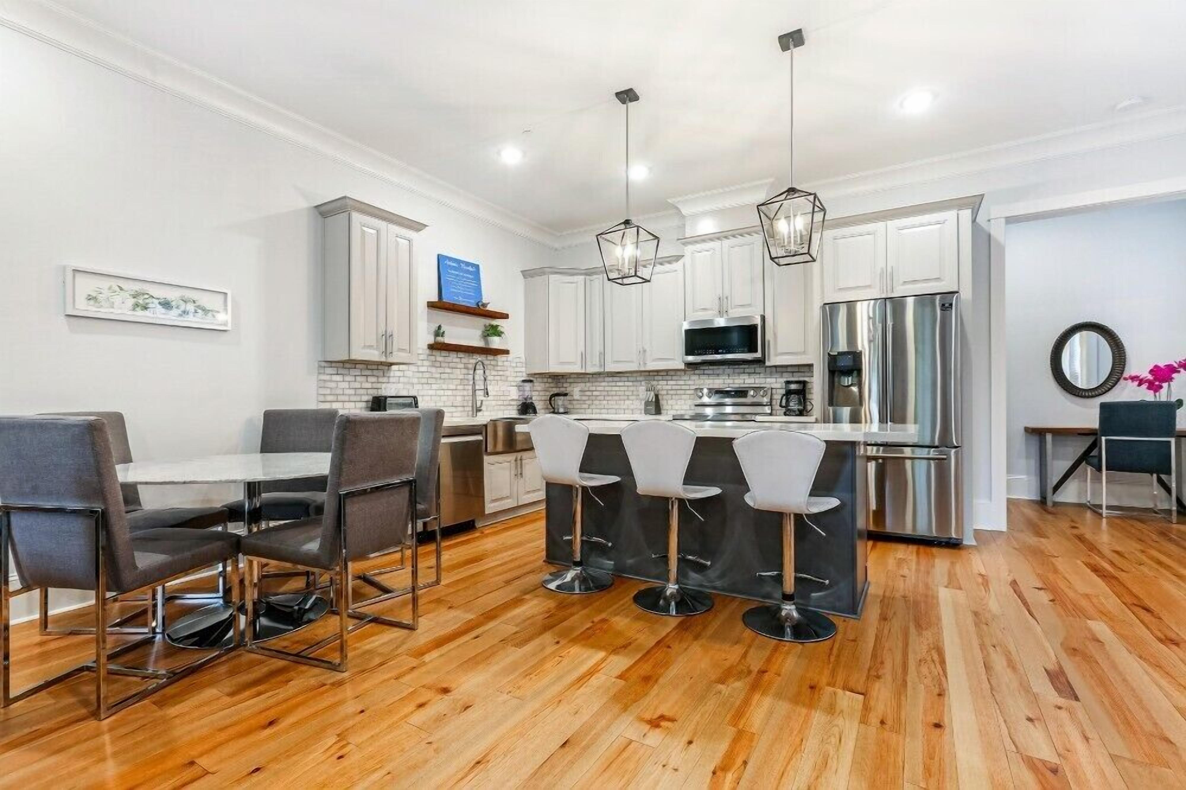 A modern kitchen with white cabinets, a central island with bar stools, and a dining area with a table and chairs.