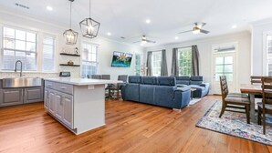 A spacious living area with a kitchen, a blue sofa set, wooden flooring, and a dining table with chairs. - 15% OFF Monthly | 10% OFF Weekly- Chic Urban Retreat w Pool Steps to St. Charles Ave and (New Orleans)