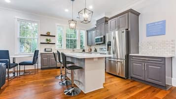 A modern kitchen with a central island, bar stools, stainless steel appliances, and a view of greenery outside.