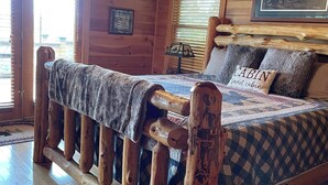 Une chambre dans une cabane en bois, avec un lit, un ventilateur de plafond et une fenêtre avec des stores.