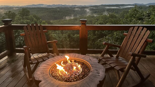 Une terrasse dotée d’un foyer et de deux chaises en bois, offrant une vue sur un paysage montagneux.