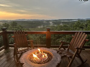 Eine Terrasse mit einem Feuerkorb und zwei Holzstühlen, mit Blick auf eine Berglandschaft.