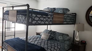 A bunk bed with patterned bedding, a bedside lamp, a clock, and a map on the wall.