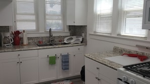 A kitchen with white cabinets, a granite countertop, a sink, a coffee maker, a toaster, and a stove.