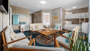 Habitación de hotel compacta con kitchenette, sofá, mesa de centro de madera y litera.