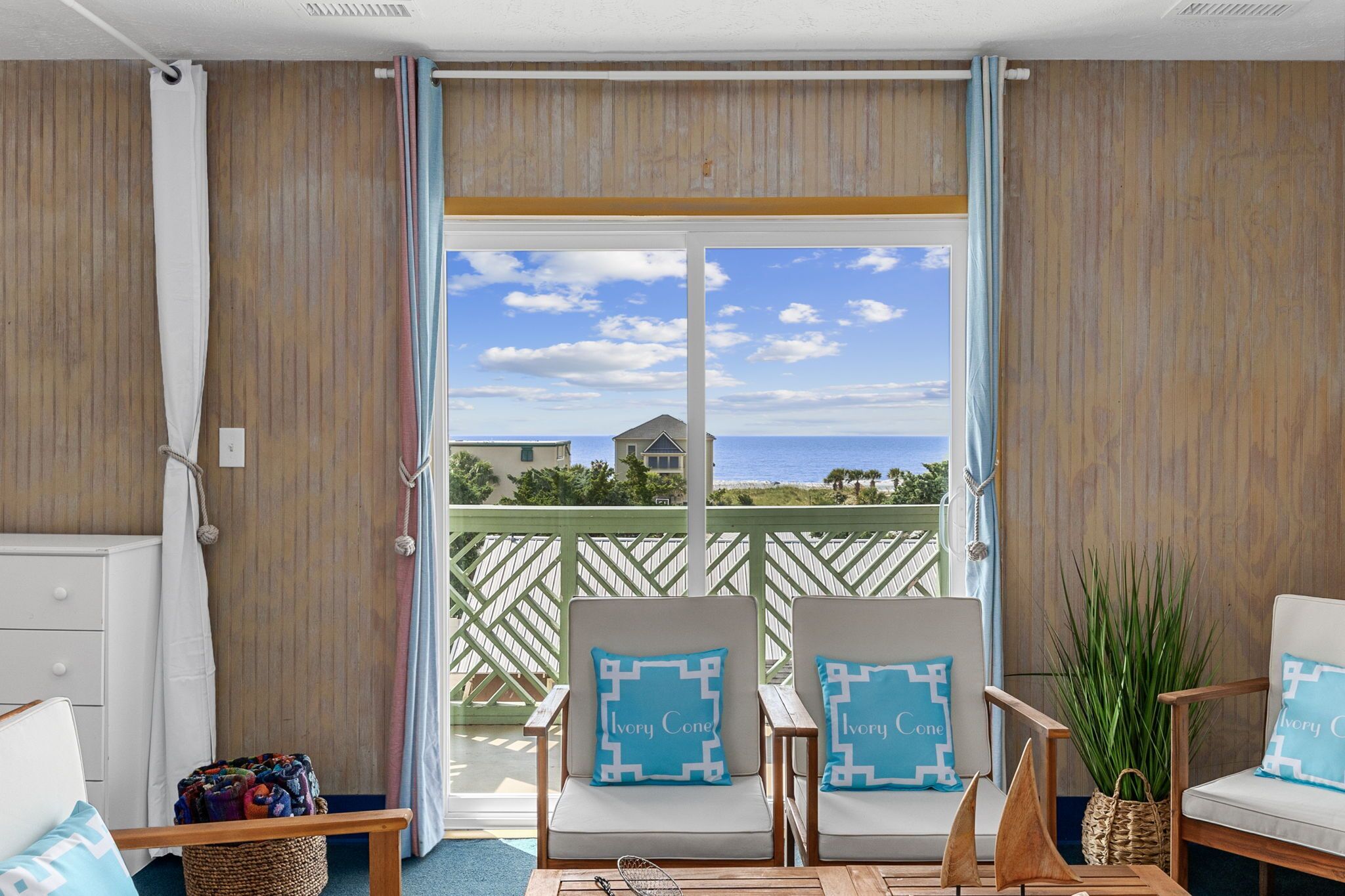 A balcony with two chairs, a small table, and a view of the beach and ocean.