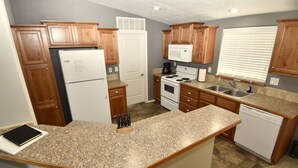 Una cocina compacta con armarios de madera, encimera de granito, refrigerador, microondas, estufa, pileta y lavavajillas.