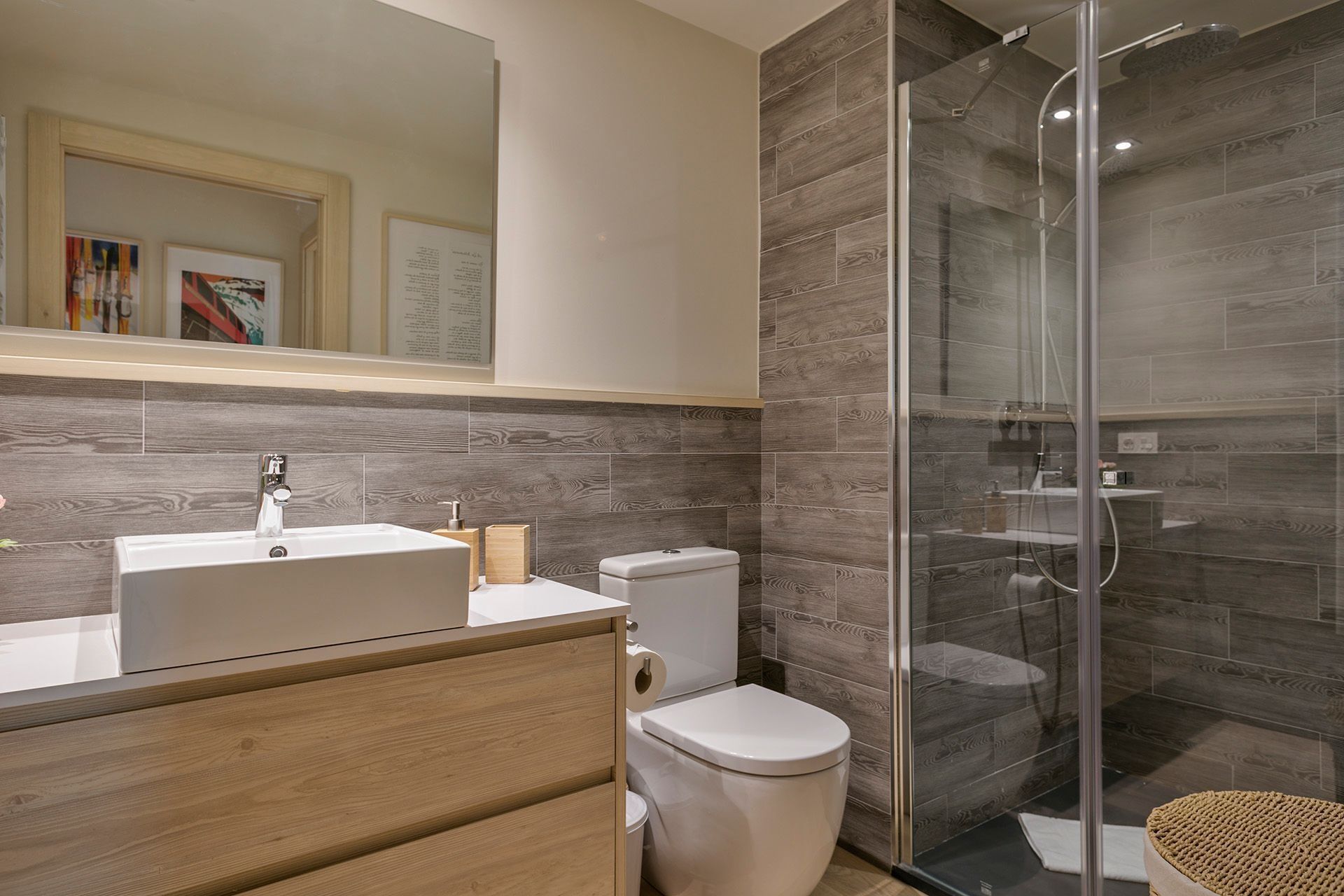Un baño moderno con cabina de ducha de vidrio, tocador de madera y inodoro blanco.