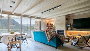 Un salón moderno con un ventanal grande, un sofá azul verdoso, suelo de madera y un televisor de pantalla plana montado en la pared.