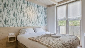 Un dormitorio con cabecera de madera, una cama grande con sábanas blancas, un edredón beige suave y una ventana con cortinas traslúcidas.