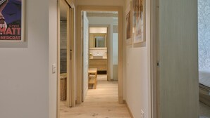 Un pasillo que conduce a un baño con espejo, lavabo y una cama al fondo.