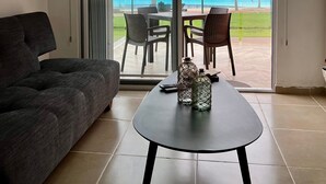 Uma sala de estar moderna com um sofá, uma mesa e vista para uma piscina e edifícios através de amplas portas deslizantes.