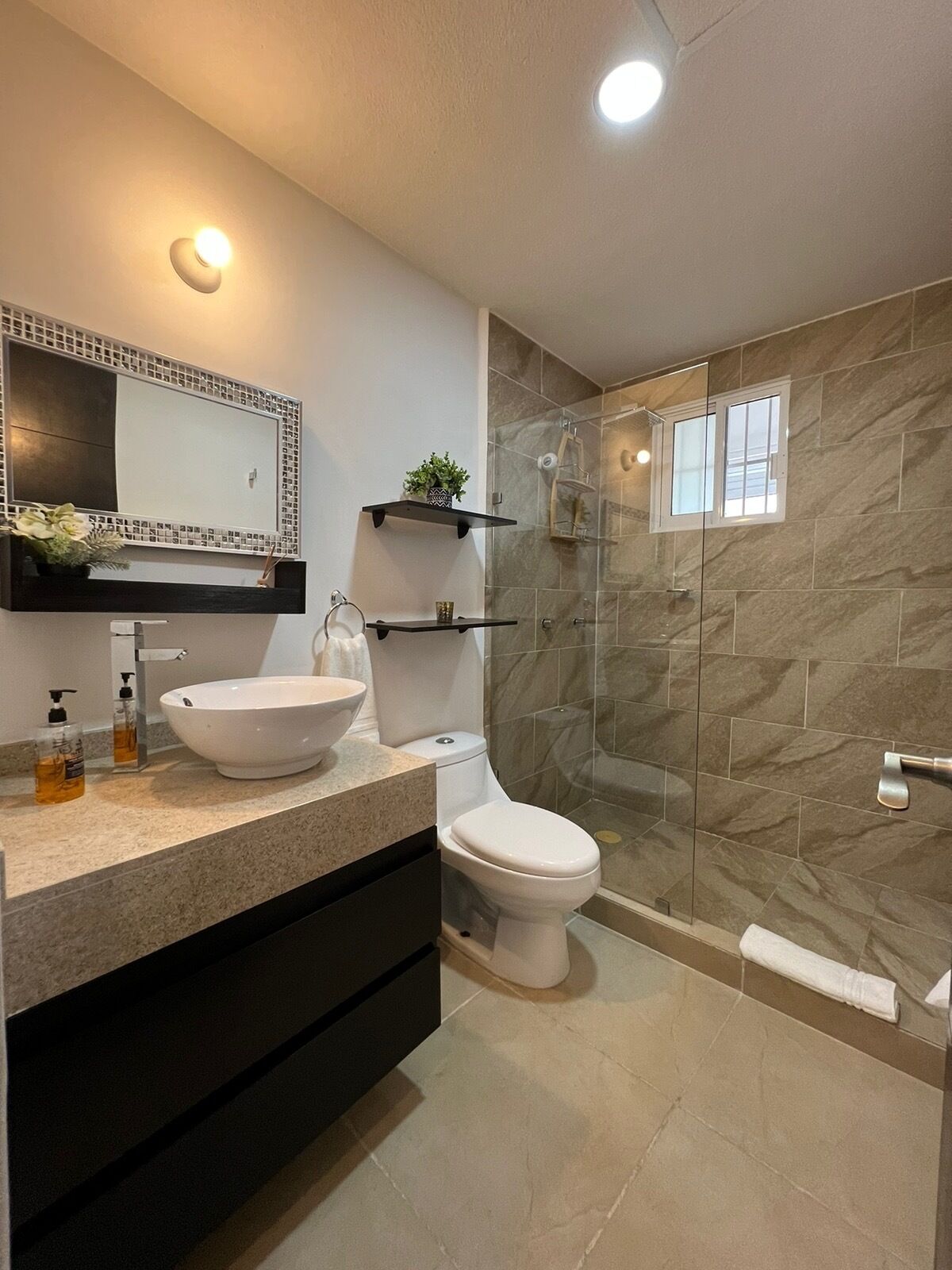 Un baño moderno con un espejo grande, un lavabo sobre encimera, un inodoro y una ducha con mampara de vidrio.