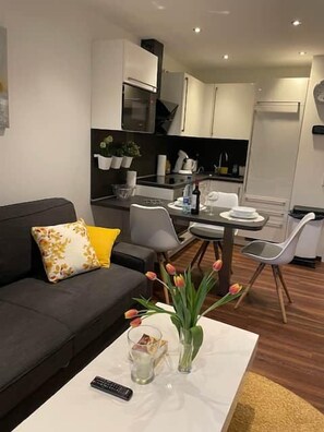 En moderne stue med en grå sofa, et sofabord med en fjernbetjening og en vase med tulipaner.