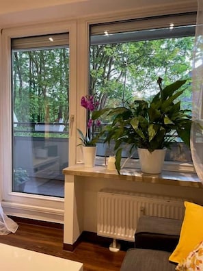 Une pièce avec une grande fenêtre, un radiateur et un canapé agrémenté d’un coussin jaune.