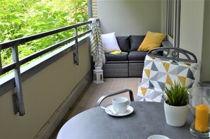 A balcony with a sofa, cushions, a table with a cup and saucer, a potted plant, and a candle.