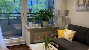 A modern living room with a sofa, a coffee table with a vase of flowers, and a view of greenery outside. - Cozy and modern apartment in green top location Münst (Münster)
