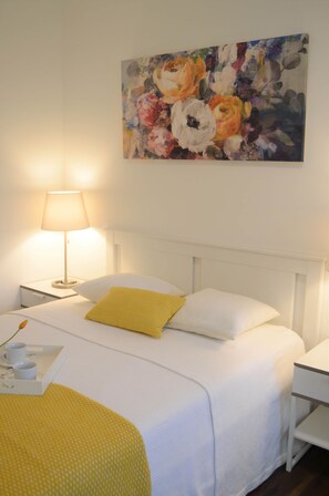 A neatly made bed with a white headboard, a yellow pillow, and a white pillow. There is a painting on the wall above the bed.
