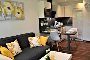 A modern living room with a black sofa, floral cushions, and a dining area with a table and chairs.