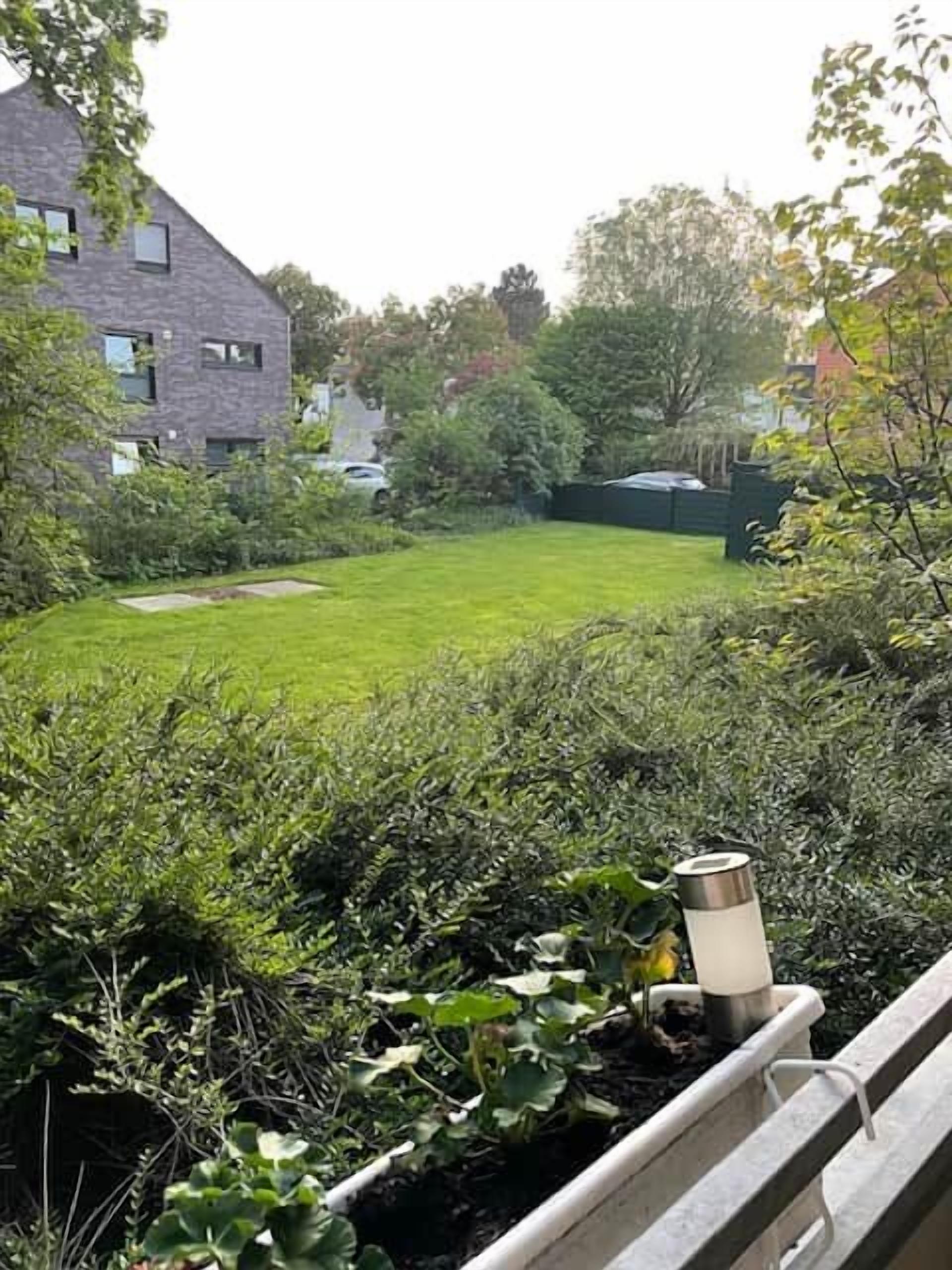 Een tuin met gras, verschillende struiken en een metalen waterreservoir.