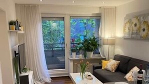 A modern living room with a sofa, coffee table, and dining table. There are plants on the windowsill and a TV on a stand. - Cozy and modern apartment in green top location Münst (Münster)