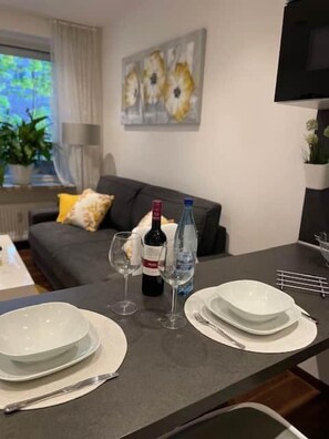 En spiseplads med et bord dækket til to personer, inklusive tallerkener, glas og en vinflaske.
