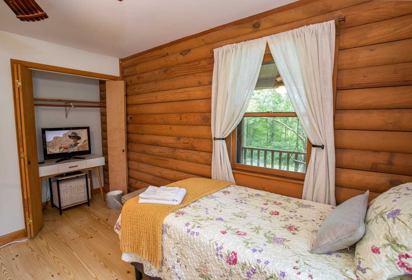 A cozy cabin room with a bed, a TV, and a window with curtains.
