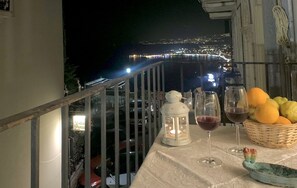 A balcony with a table set for two, featuring a wine glass, a lantern, and a basket of fruit. - A view of paradise (Taormina)