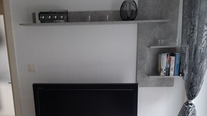 Un téléviseur à écran plat posé sur un meuble blanc, agrémenté d’un vase décoratif et de quelques livres.