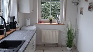 Une cuisine moderne dotée d’une grande fenêtre, de meubles blancs, d’un évier encastré et d’un radiateur.