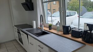 Une cuisine moderne équipée d’un évier encastré, d’une cuisinière et d’un plan de travail sur lequel se trouvent une machine à café et une bouilloire.