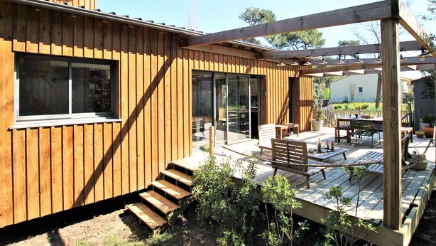 A wooden house with a deck, outdoor seating, and a sliding glass door. - Villa Les Hibiscus - 500m from the beach - authentic style and design for 8 (Longeville-sur-Mer)