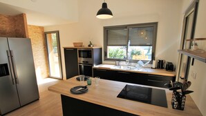 A modern kitchen with a central island, stainless steel appliances, and a large window with blinds. - Villa Les Hibiscus - 500m from the beach - authentic style and design for 8 (Longeville-sur-Mer)