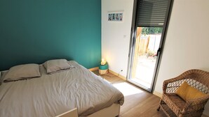 A bedroom with a bed, a wicker chair, and a sliding glass door leading to an outdoor area. - Villa Les Hibiscus - 500m from the beach - authentic style and design for 8 (Longeville-sur-Mer)