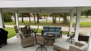 A covered patio with wicker furniture, a fire pit, and a grill. - Camp Coastal Escape with perks and discounts!! (Jacksonville)