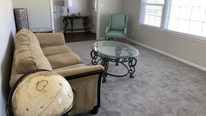 A living room with a beige sectional sofa, a glass coffee table, a globe, a teal armchair, and a lamp on a small table. - Camp Coastal Escape with perks and discounts!! (Jacksonville)
