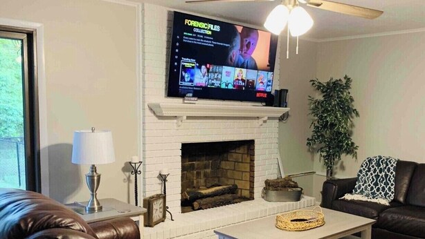 A living room with a fireplace, a television mounted above it, a ceiling fan, and leather sofas. - Camp Coastal Escape with perks and discounts!! (Jacksonville)