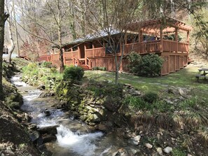 Uma cabana rústica com um deck de madeira e um pequeno riacho correndo por um jardim.