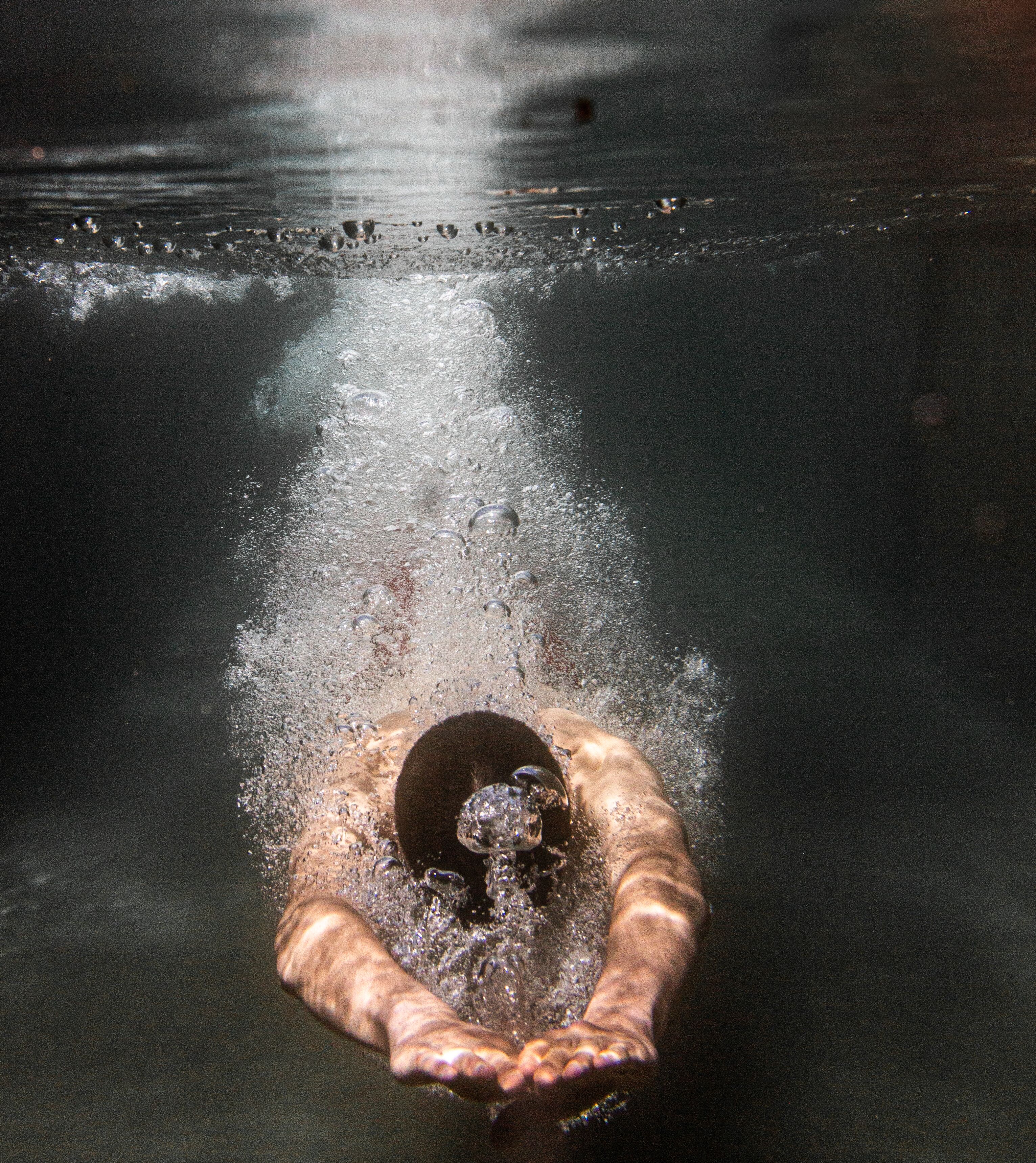 A hand reaching into a body of water, creating ripples and bubbles.
