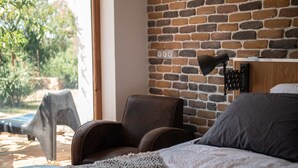 A bedroom with a brick wall, a bed, a chair, and a lamp. - 4u Bed & Spa (Opoul-Perillos)
