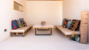 A small, cozy room with a wooden ceiling, a white table, two cushioned seating areas with colorful pillows, and a small potted plant. - 4u Bed & Spa (Opoul-Perillos)