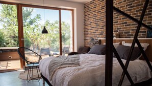A modern bedroom with a large bed, a brick wall, and a view of greenery through a sliding glass door. - 4u Bed & Spa (Opoul-Perillos)
