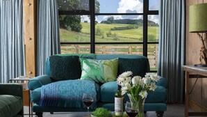 Un salón acogedor con un sofá color turquesa, una mesa de madera con bebidas y vistas a un paisaje verde a través de amplios ventanales.